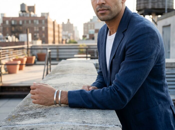 Homme portant des bracelets fins en argent empilés sur un rooftop urbain contemporain