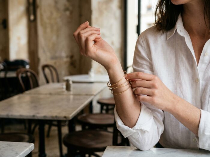Bracelets fins empilés en or sur le poignet d'une jeune femme dans un café parisien minimaliste