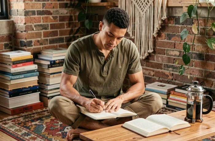 Homme écrivant dans un journal intime dans un appartement bohème décoré de livres et plantes, style de vie créatif